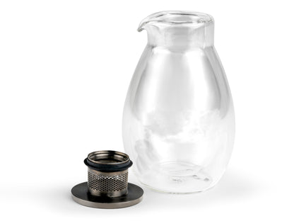 Clear glass handle-less teapot with metal lid and filter removed on a white background