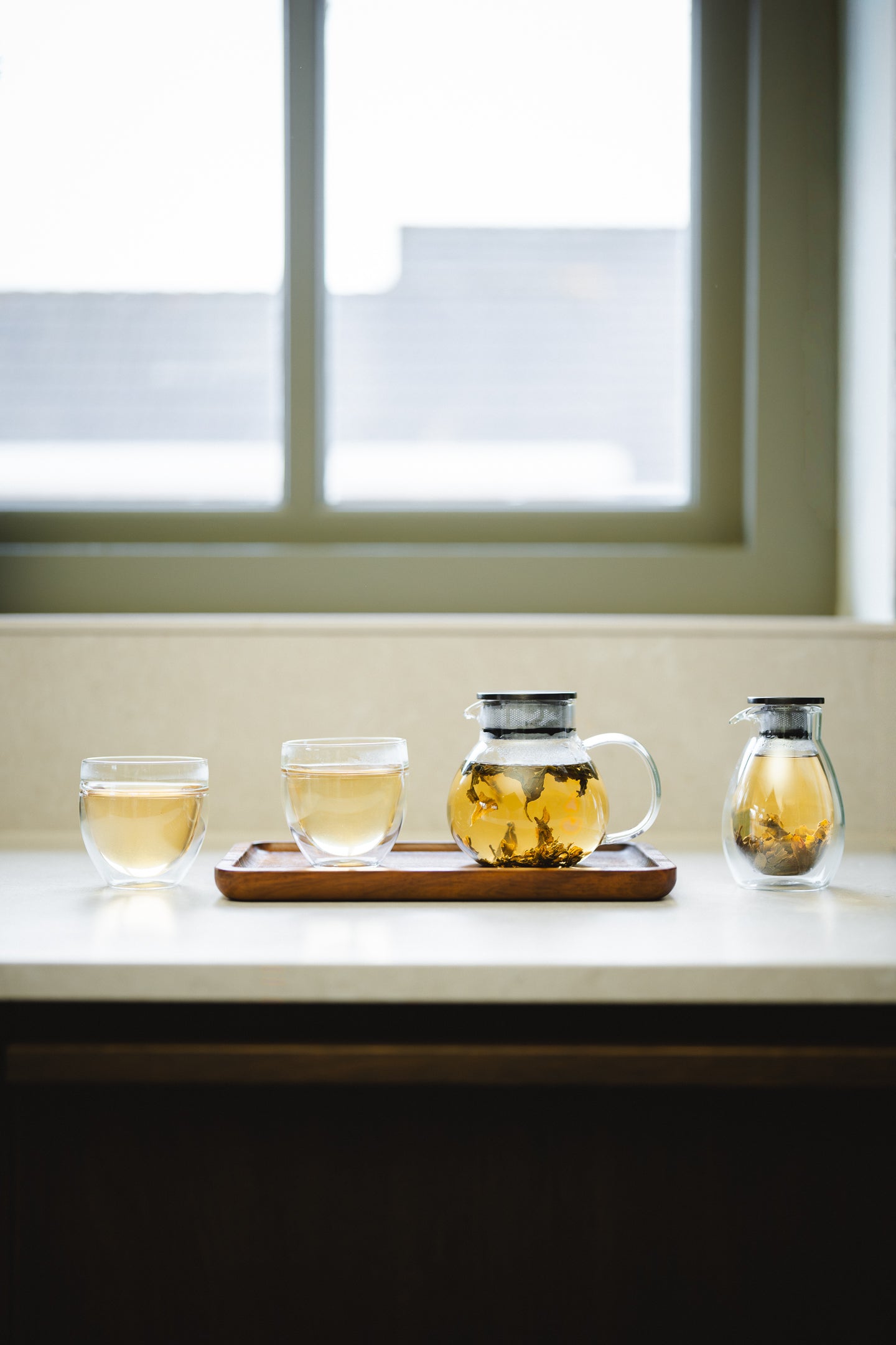 Tea-making setup with filled glass teapots and cups on a windowsill.