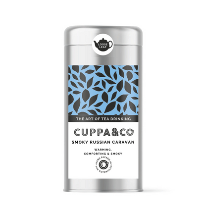 A silver caddy tin of tea labelled 'CUPPA & CO' 'Smoky Russian Caravan' with a leaf pattern on the label and a separate round label with a black teapot and the words LOOSE LEAF.