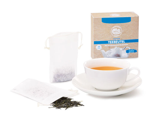 Tea cup with saucer, compostable paper tea filter bags with drawstring, and a box of tea bags on a white background