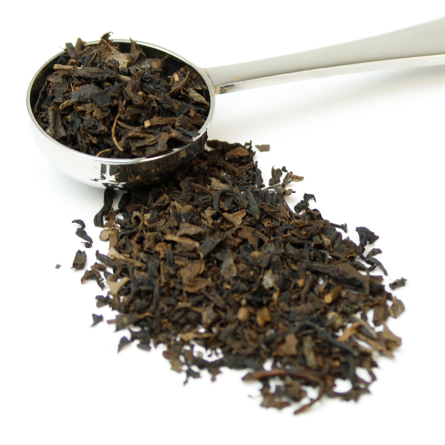 Small black tea leaves in a silver teaspoon on a white background