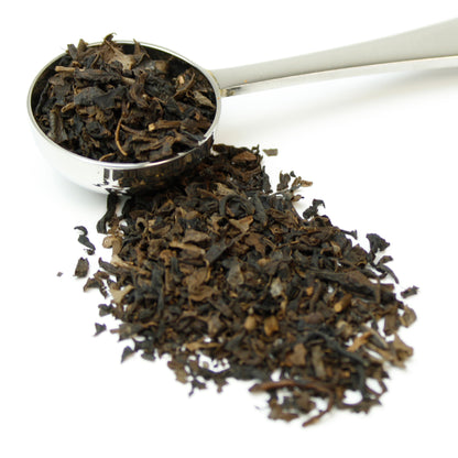 Small black tea leaves in a silver teaspoon on a white background