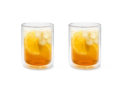 Two clear glass tumblers of iced tea with lemon slices on a white background