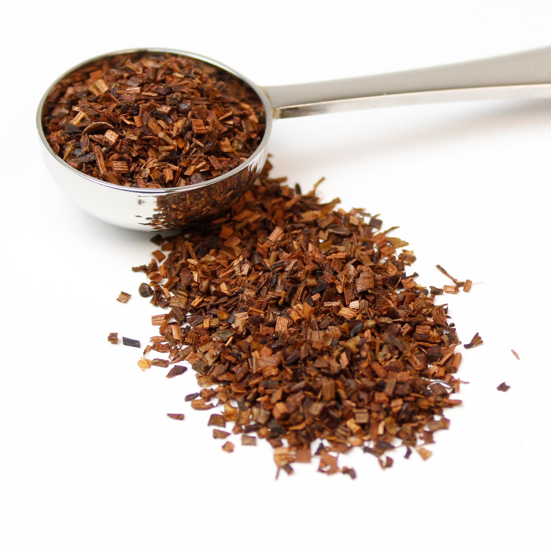 Loose Honeybush tea pictured in a silver spoon spilling over on to a white background