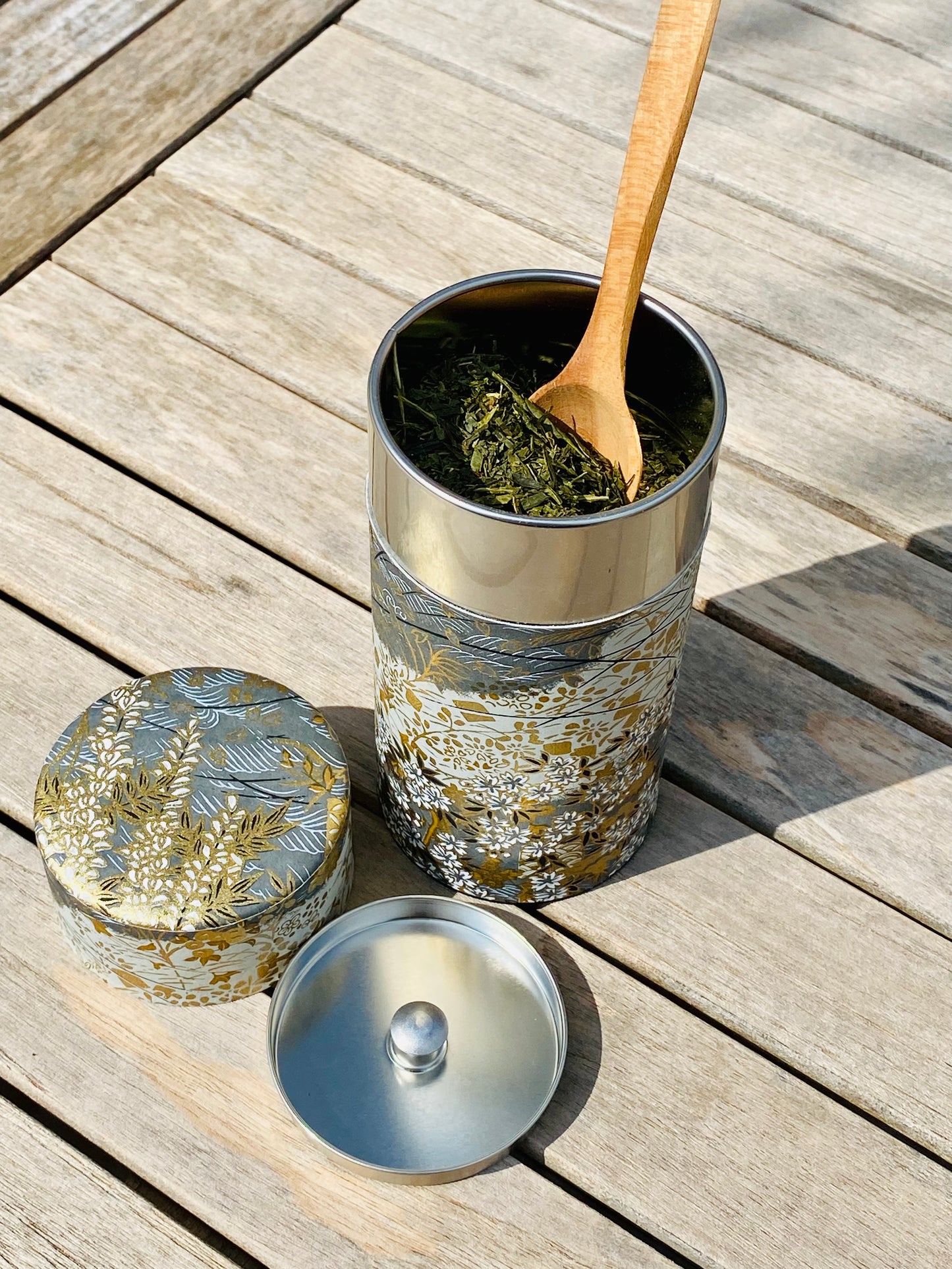 Tea canister filled with tea and with wooden spoon on a wooden surface