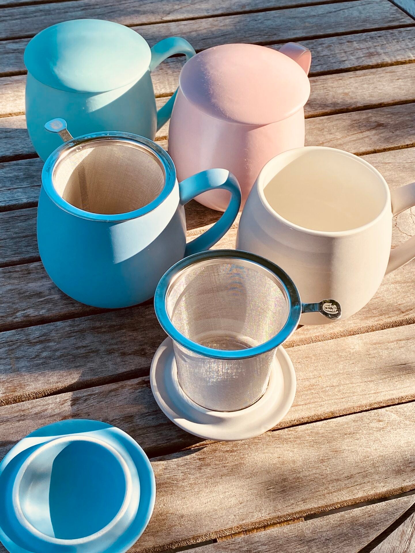 Lifestyle image of set of colorful mugs with lids and tea infusers on a wooden surface