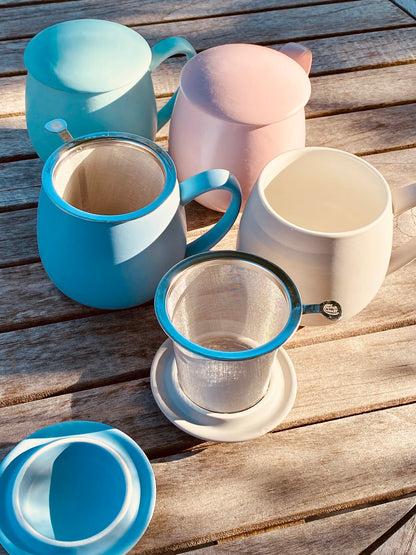Lifestyle image of set of colorful mugs with lids and tea infusers on a wooden surface