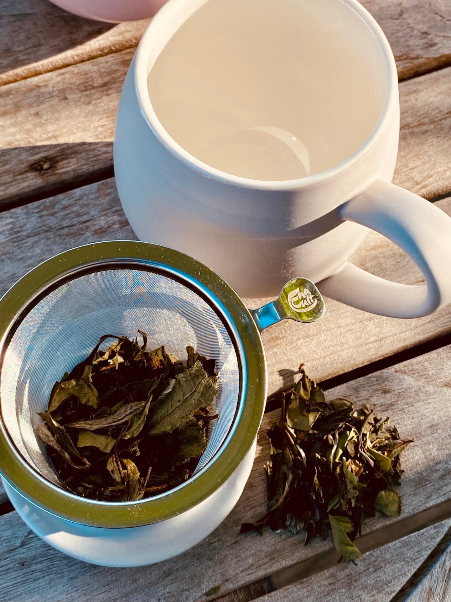 Grey porcelain mug with white interior with tea leaves in a metal strainer on a wooden surface