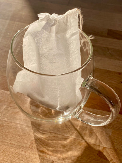 compostable paper tea filter inside a clear glass cup sitting on a wooden surface.