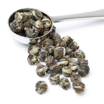 A silver teaspoon containing rolled Jasmine Pearls tea on a white background