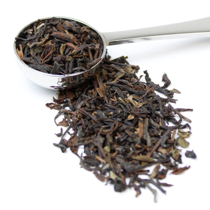 Loose black tea leaves in a teaspoon and on a white background.
