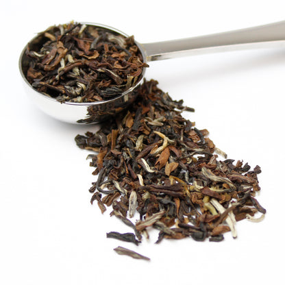 Silver teaspoon containing black loose leaf tea on a white background