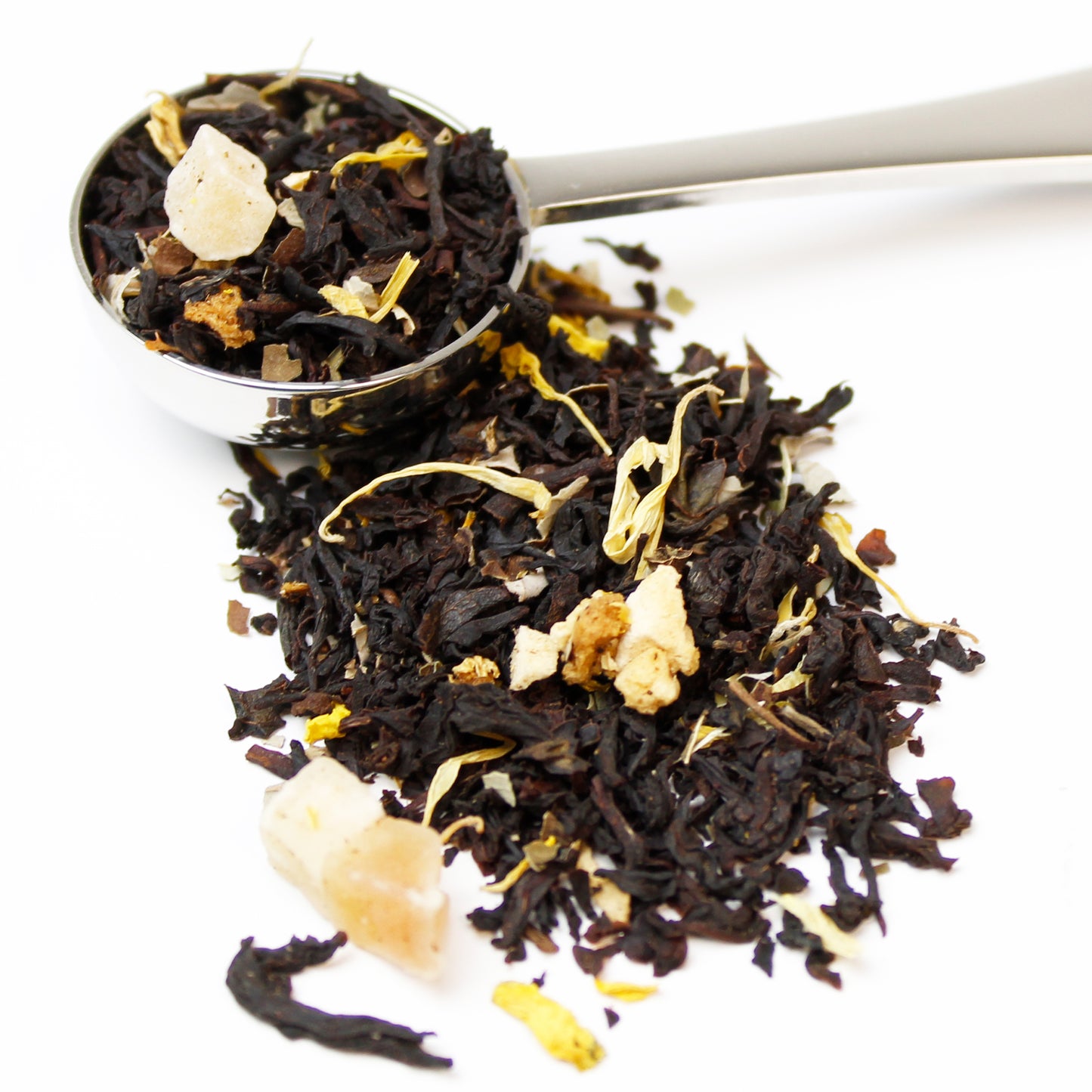 A silver teaspoon of loose black tea with pieces of dried yellow fruit and yellow flower petals on a white background.