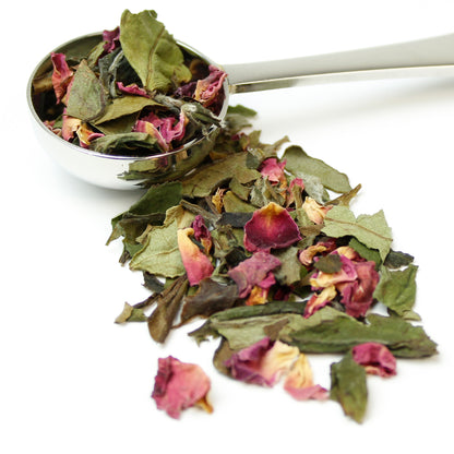 Loose white tea leaves blended with rose petals spilling out of a silver spoon on a white background