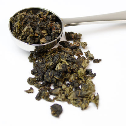 Silver teaspoon filled with Phoenix Oolong tea spilling over on to a white background
