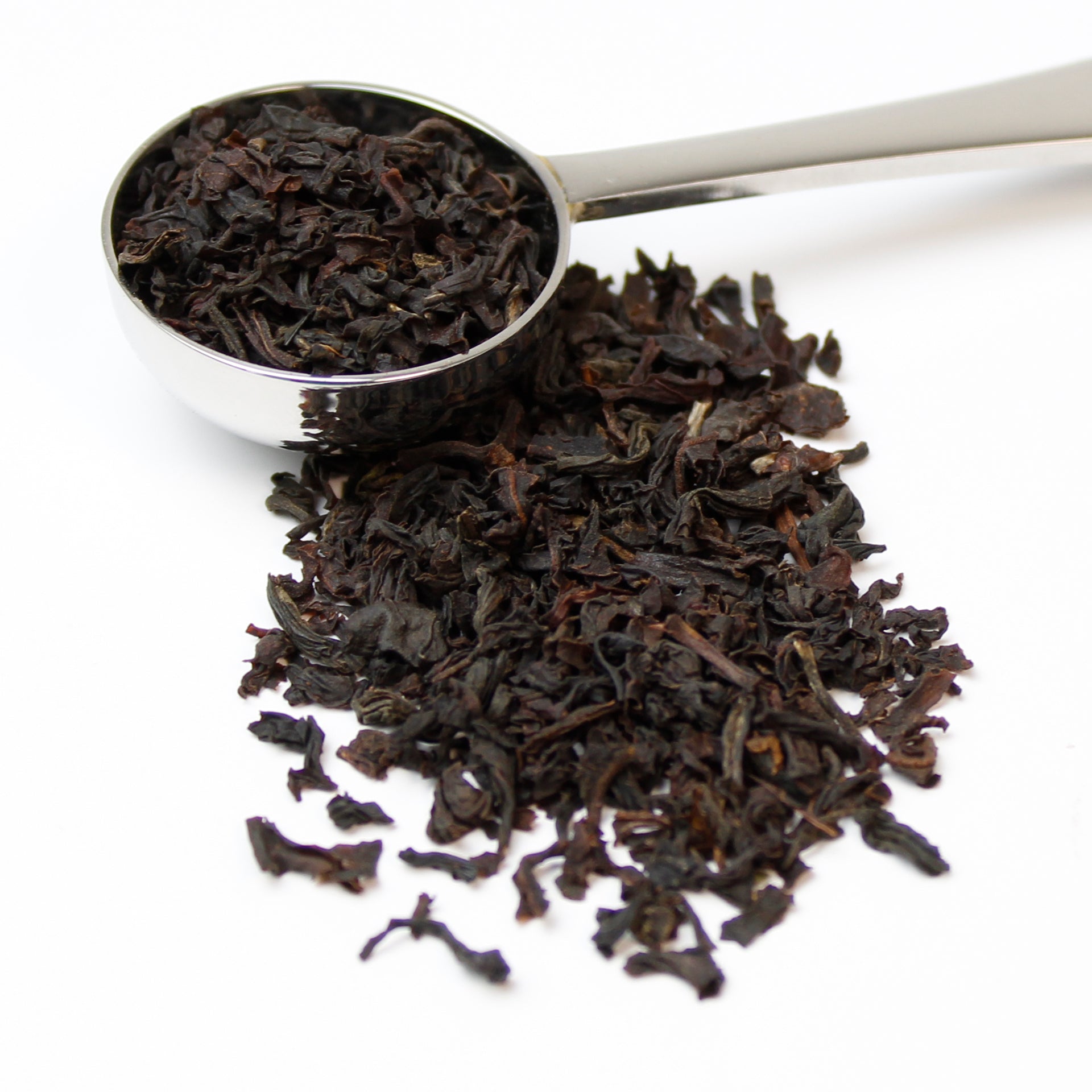 Small silver teaspoon of fine loose tea leaves overflowing onto a white surface.