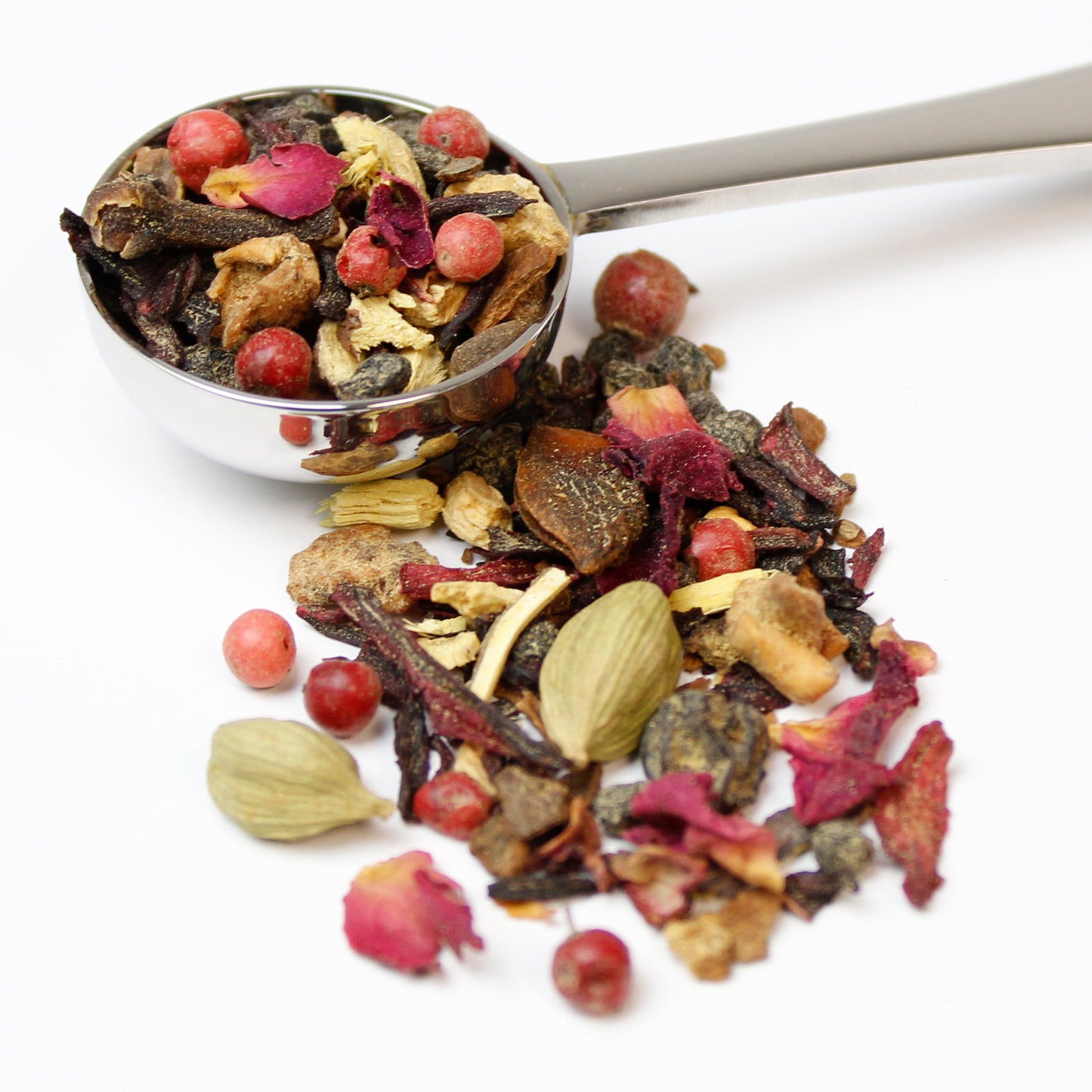 Loose blend of fruit, spices and rose petals in a silver teaspoon on a white background