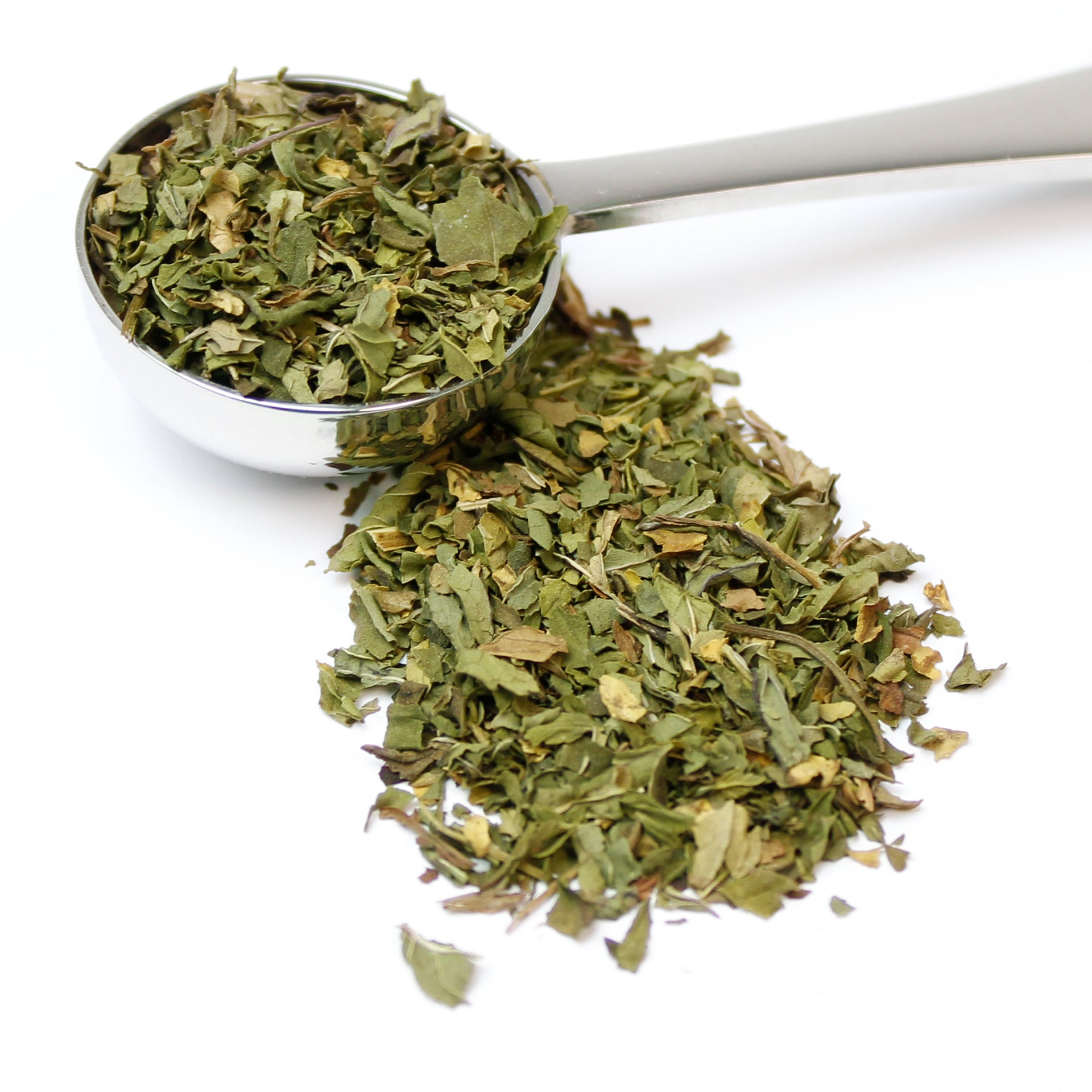 Silver spoon of dried spearmint leaves spilling over on to a white background.