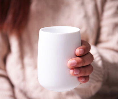 Person holding a white porcelain mug with a soft focus background